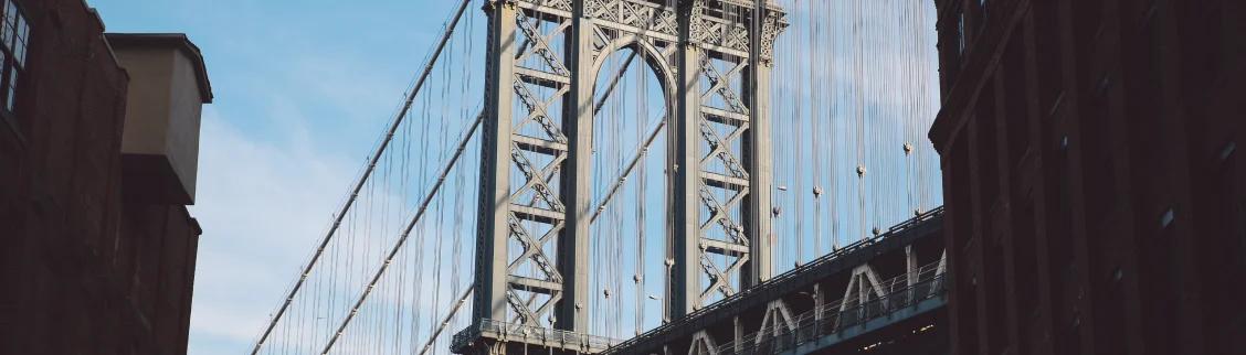 Manhattan Bridge steel towers and suspension cables framed by Brooklyn buildings under clear sky