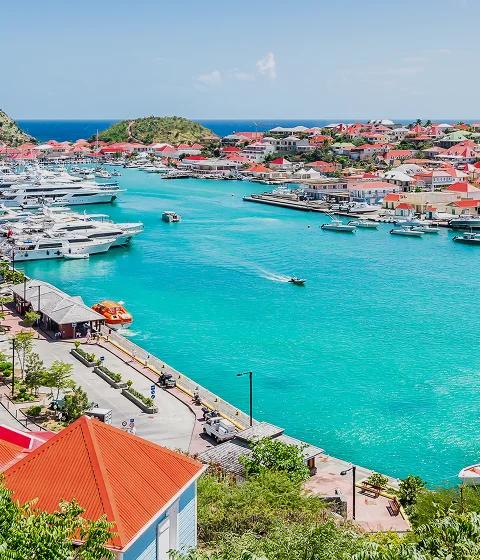 Stunning aerial view of St. Barts harbor with luxury yachts, red-roofed villas, and turquoise waters