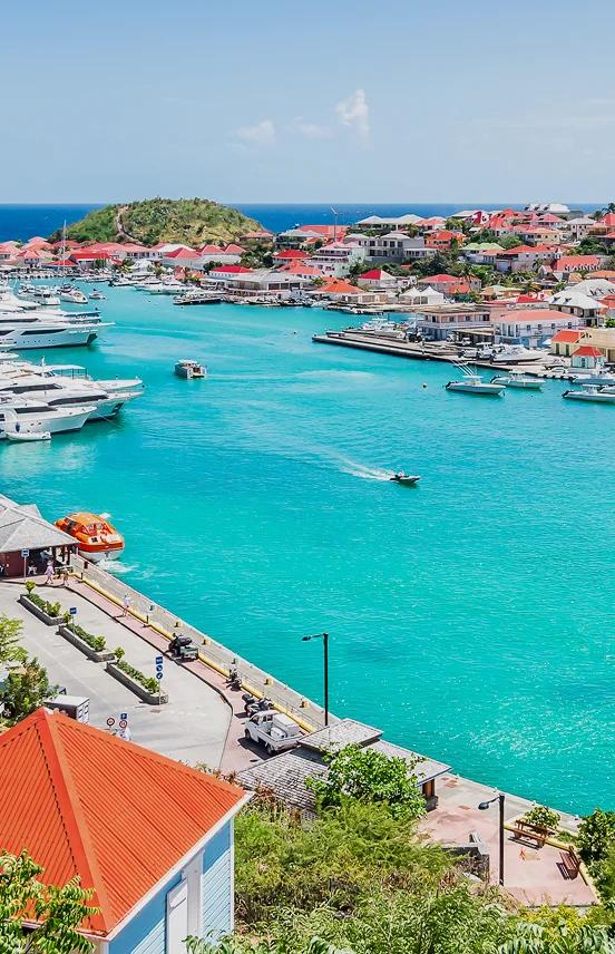 Stunning aerial view of St. Barts harbor with luxury yachts, red-roofed villas, and turquoise waters
